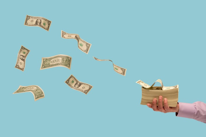 Dollar bills flying off of a stack of money.