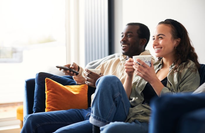 Two people sitting on a couch, watching TV.