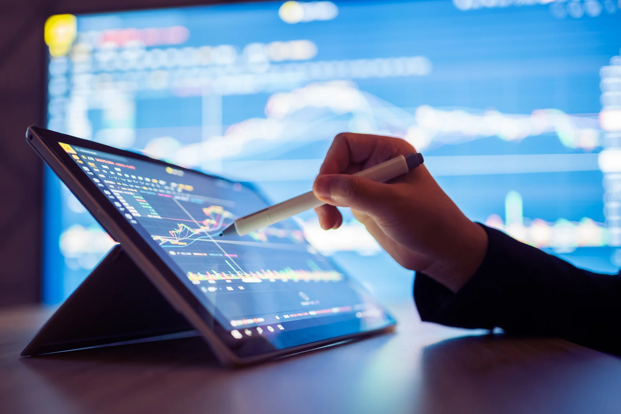 A tablet on a table with a stock chart and hand following a curve.