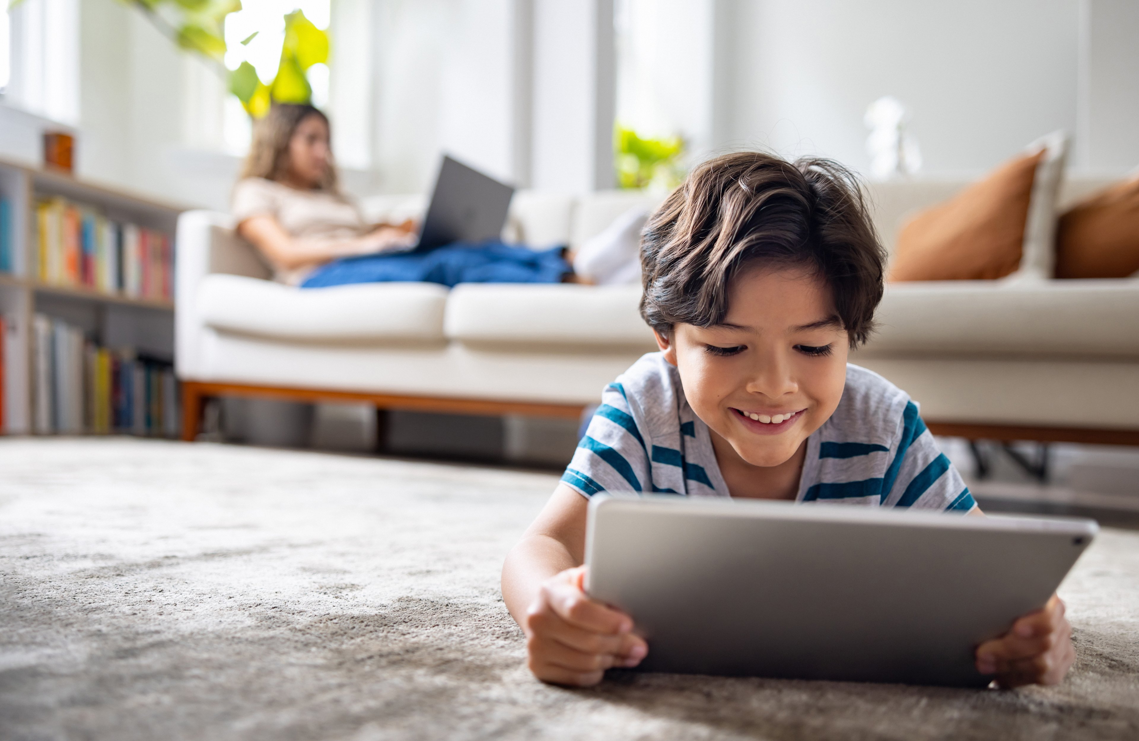 Child laying down on the floor holding a tablet.