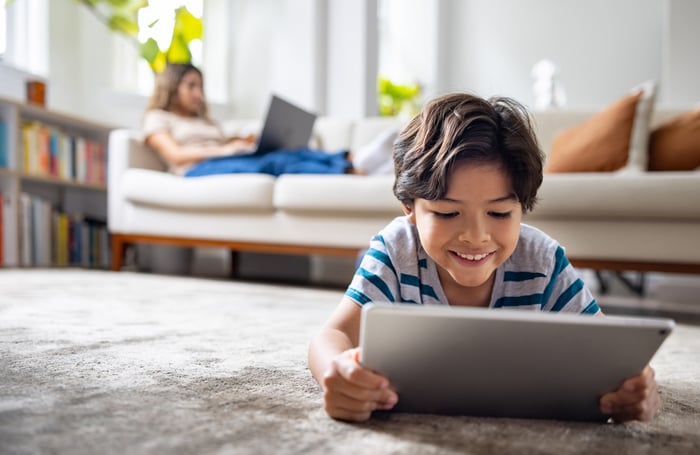 Child laying down on the floor holding a tablet.