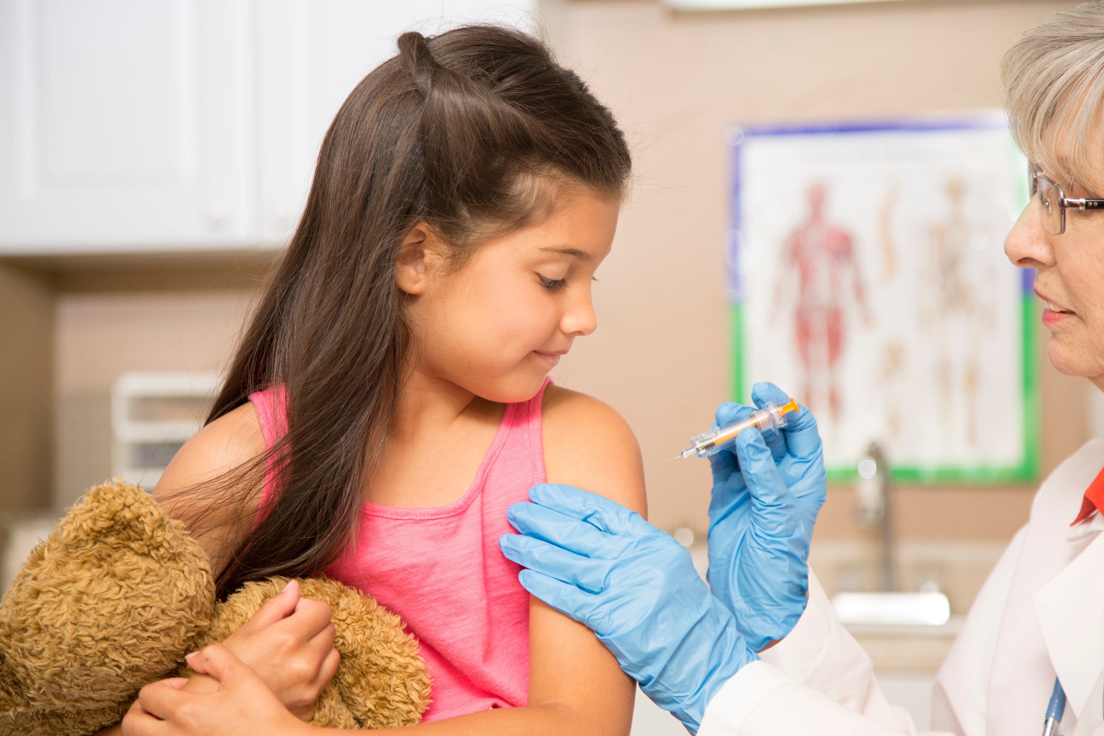 A doctor vaccinating a child holding a teddy bear.
