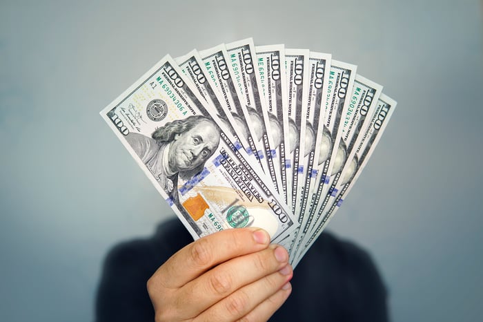 Person holding hundred-dollar bills in fan shape. 