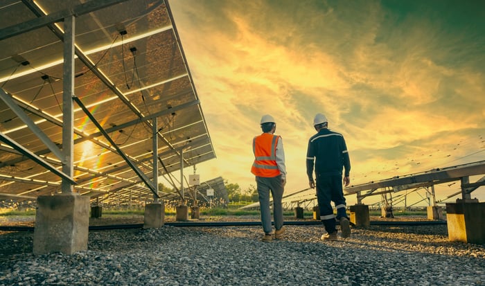 Two people walking near solar energy panels.