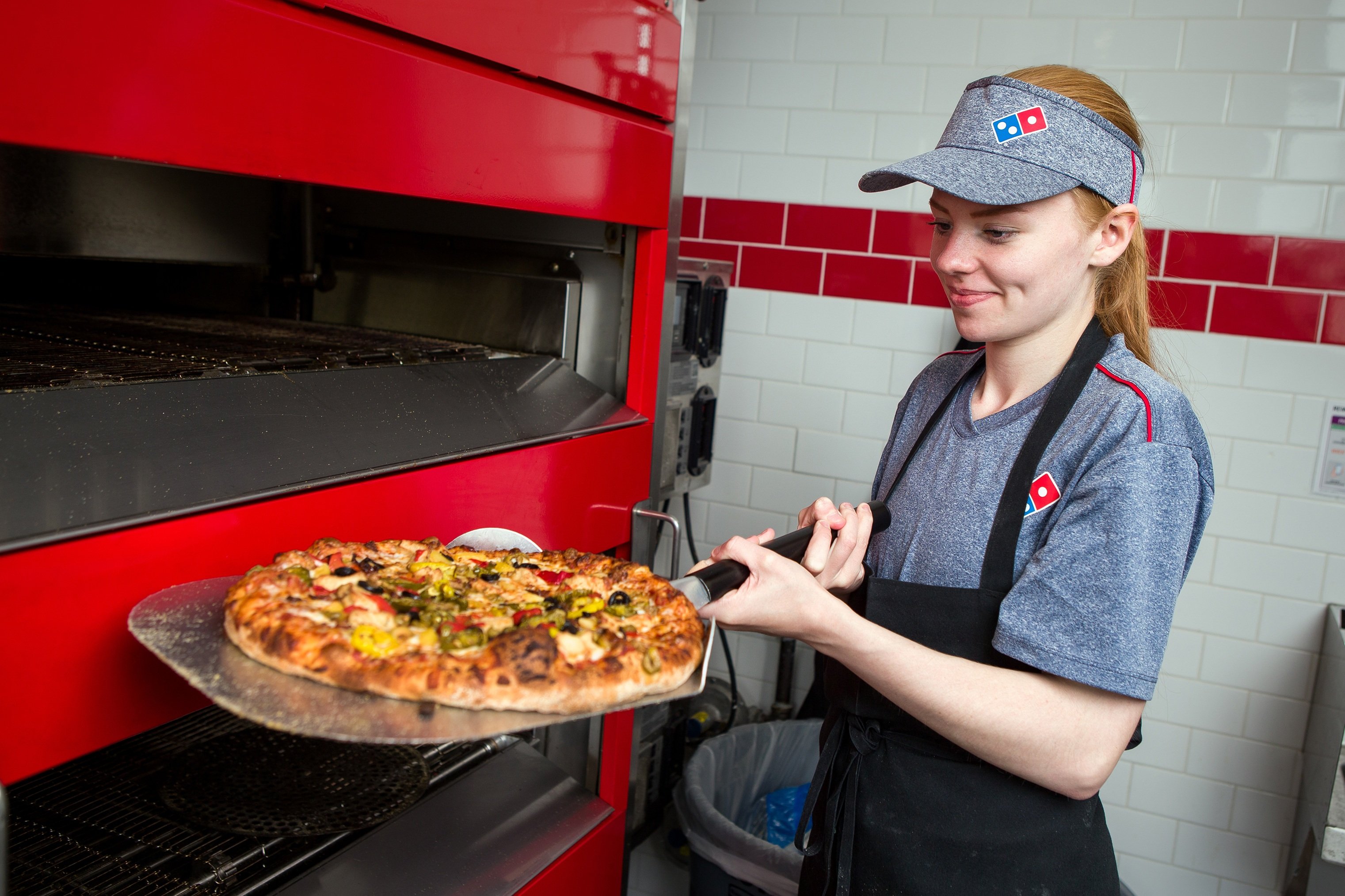 A Domino's Pizza employee taking a pizza out of an oven.