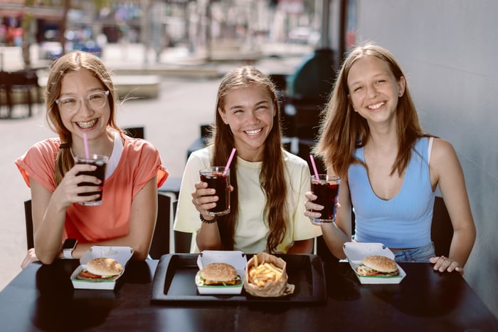 Three friends drink cola while eating fast food.