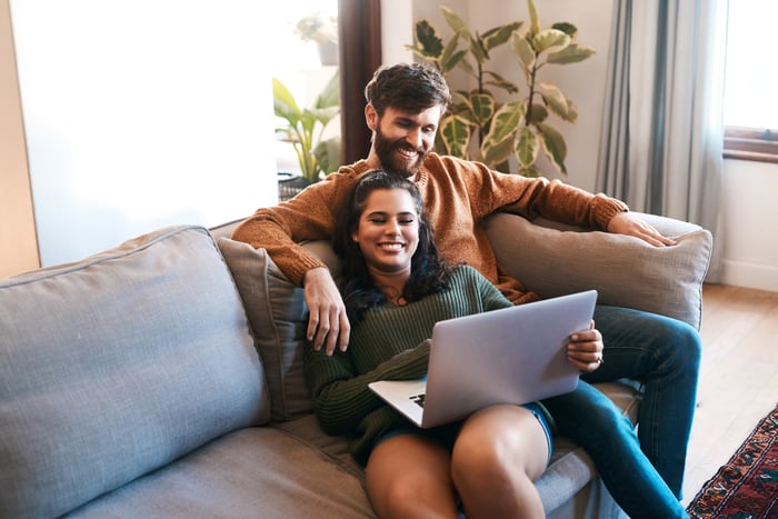 Two smiling people sitting on a couch and looking at a laptop.