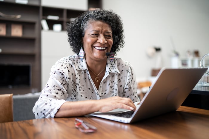 Someone is seated at an open laptop, smiling. 