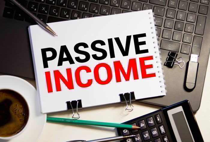 The words "passive income" boldly written on an open drawing pad resting on a keyboard with a calculator nearby.