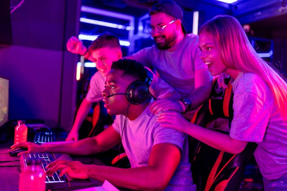 People standing near a gamer on a computer and cheering. 