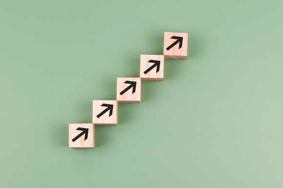 Five wooden blocks with black arrows pointing up and to the right form a line that also points up and to the right.