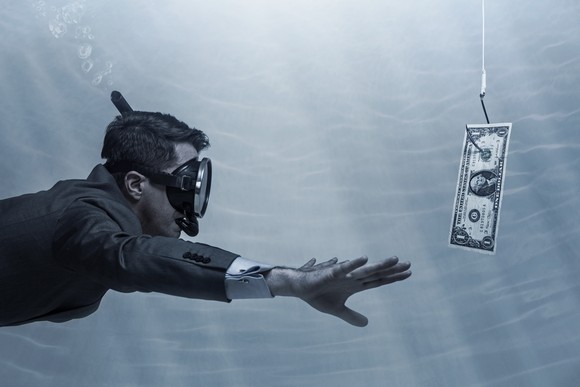Investor in suit swimming underwater toward a $1 bill on a hook.