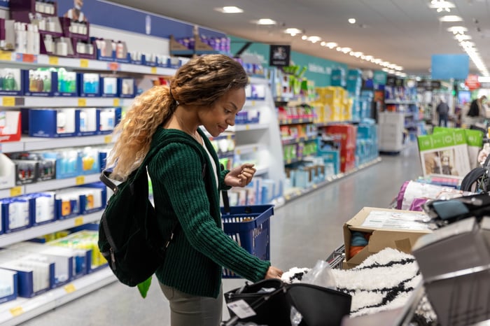 A customer carrying a shopping basket looks at goods in the aisle of a store.