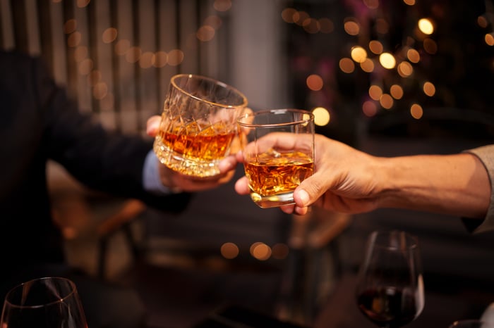 Two people in a restaurant clink their spirit-filled glasses clink. 