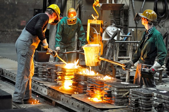 Three workers in a steel mill tending a bucket of molten steel. 