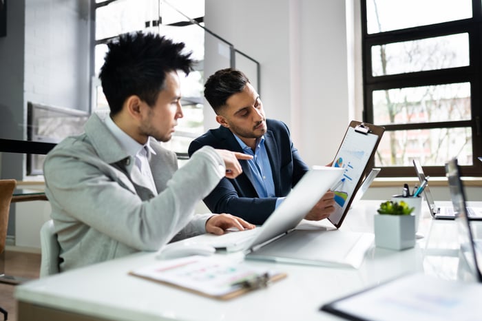Two investors looking at stock charts while sitting at a table in a very airy room.