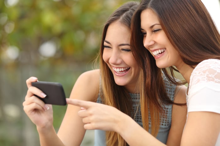 Two friends looking at the same smartphone.