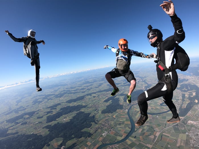 Three skydivers in the air, one with an action camera affixed to helmet.