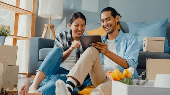 Couple in living room holding tablet and smiling at what they're seeing.