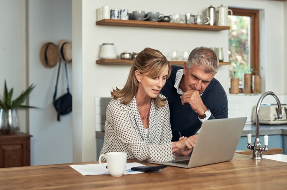 Two people using a laptop on kitchen countertop.