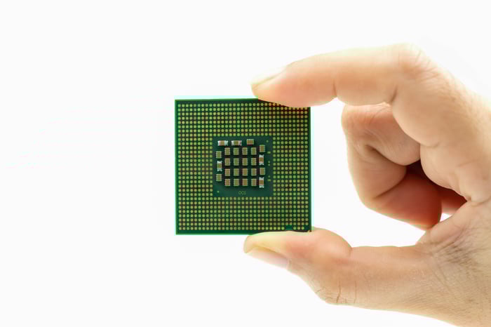 A computer chip held between a person's thumb and index finger.