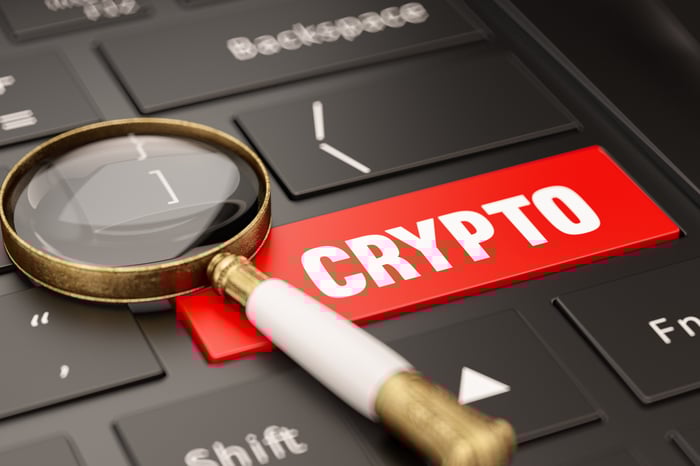 A spyglass rests on a computer keyboard, which has a large, red Crypto key.