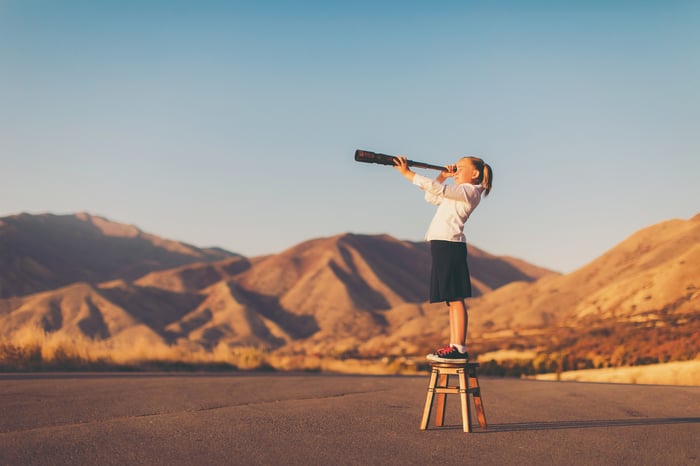 A child stands on stool and looks through a telescope.
