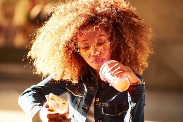 A person drinking lemonade while sitting outside and looking at their phone.
