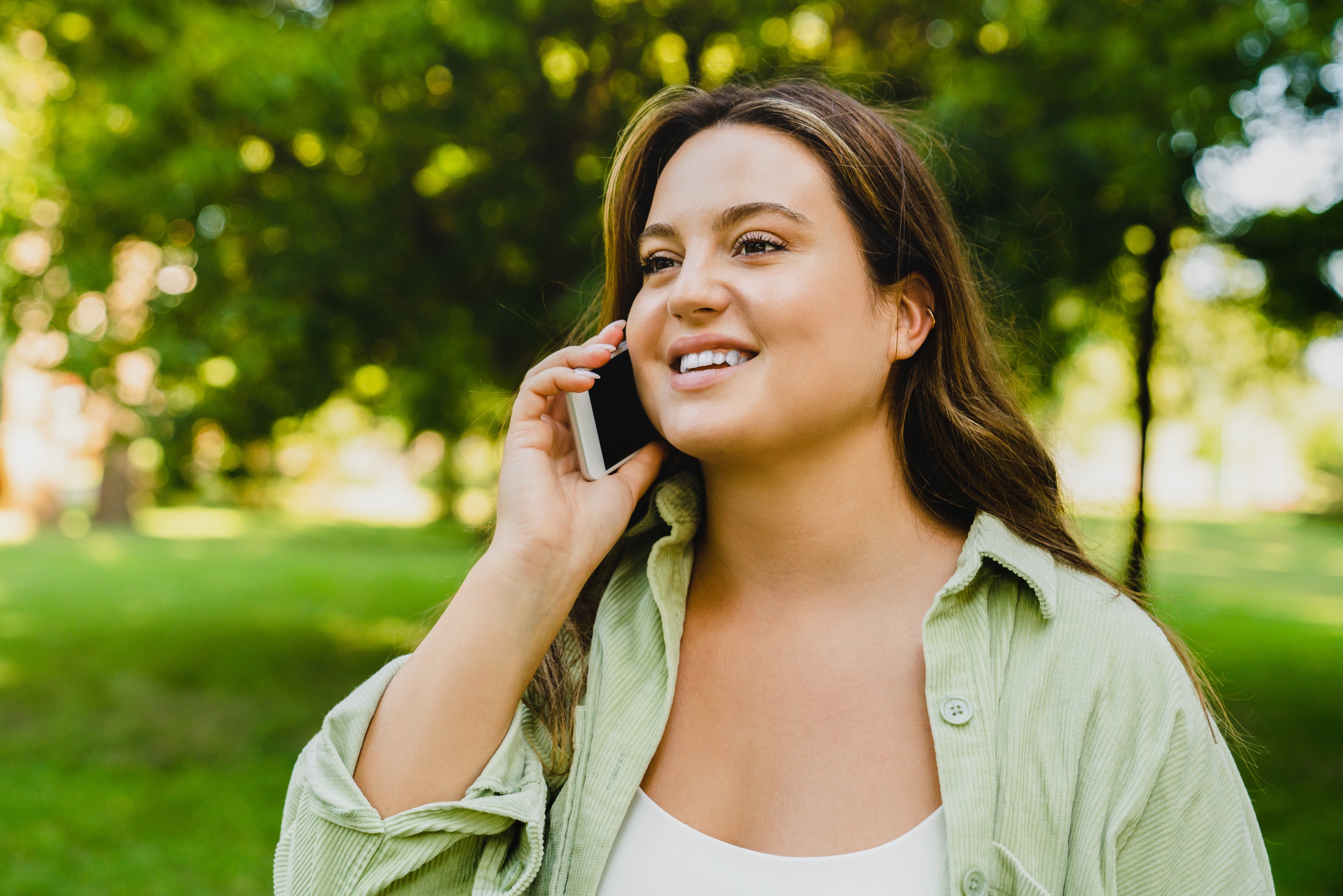 A person talking on their phone while standing outside in the park.