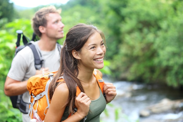 A couple is outdoors, hiking near a river -- and smiling.