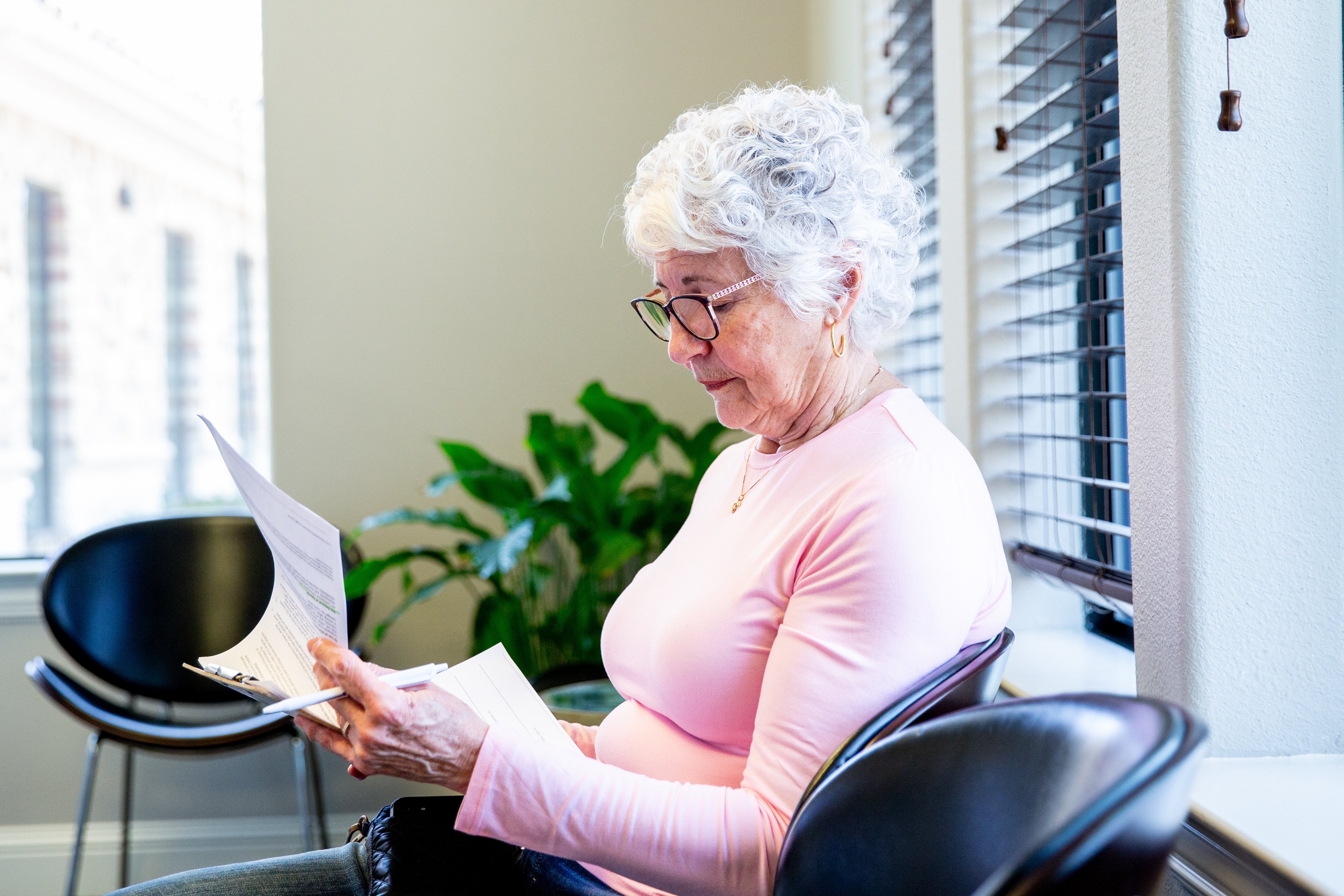 Someone sitting in a chair and reading papers on a clipboard.