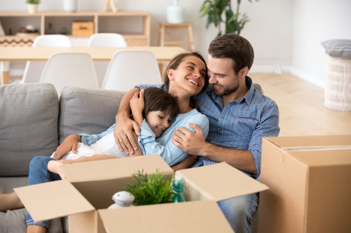Two adults and a child on a sofa, surrounded by moving boxes.