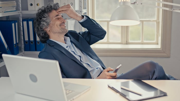 An investor sitting at a desk smiles while touching his head.