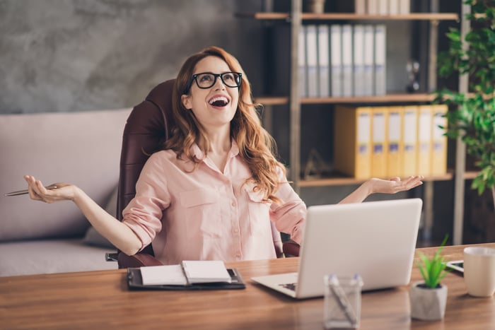 An investor expresses elation as she sits in front of her computer and a notebook in an office.