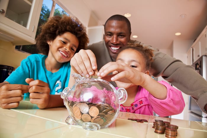 A father and his two kids save pennies in a piggy bank.