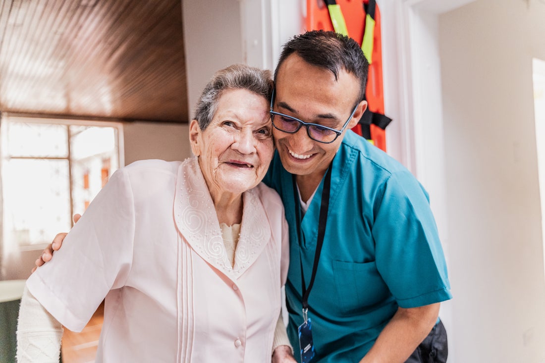 Elderly woman in a nursing home, being helped by a smiling male nurse. 