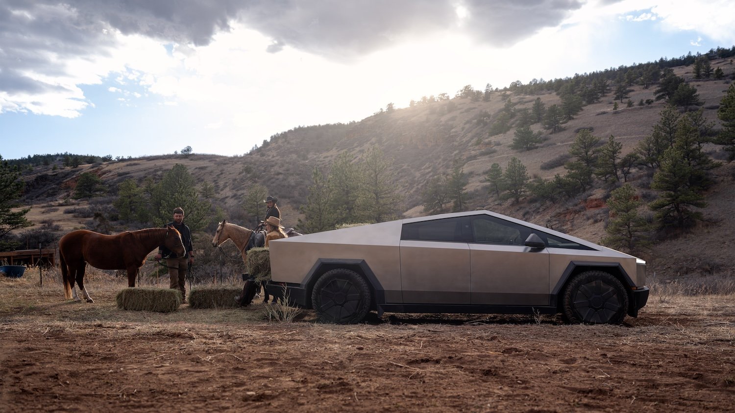 A Tesla truck next to people with horses.