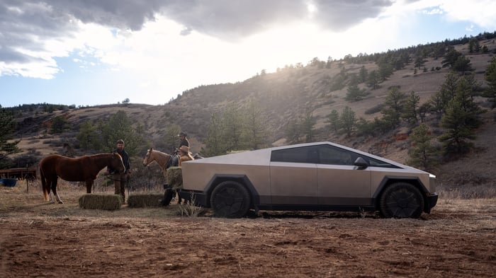 A Tesla truck next to people with horses.