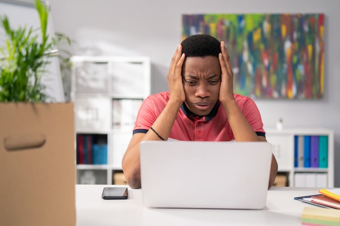 A person looks at a laptop with their face resting in their hands.