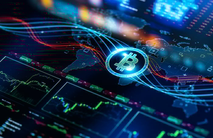 A Bitcoin logo rests on a screen with several different stock charts with trends mapped.