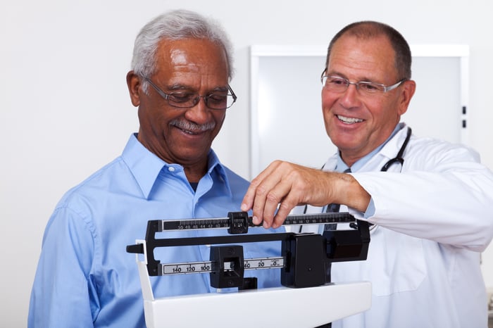 A medical professional adjusting the weights on a scale for a patient being weighed. 