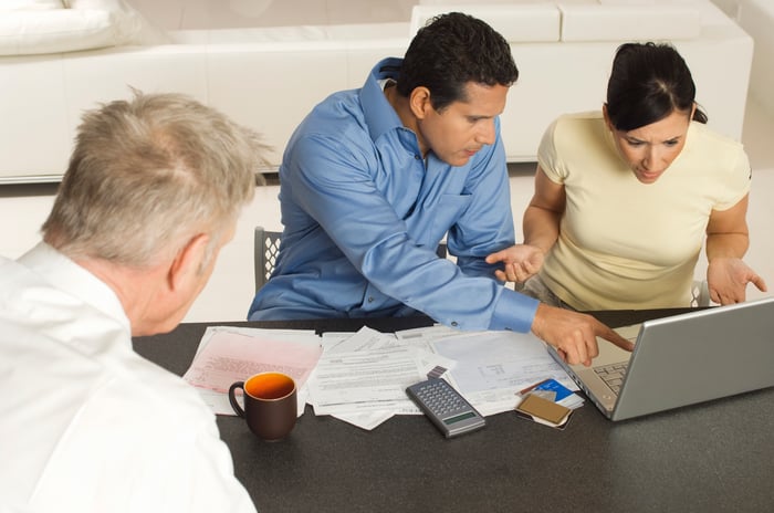 People looking at computer and working with documents at table.