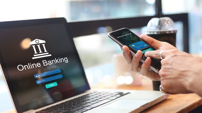 A computer that says online banking on it with a person holding a smartphone in front of it. 