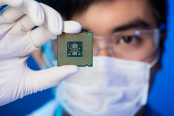 Person in glasses and mask holding an integrated circuit.