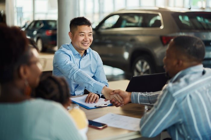 Two people shaking hands at an auto dealership.
