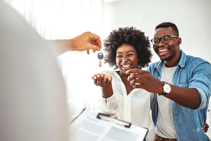 Two people hold out their hands to receive a key from a third person.