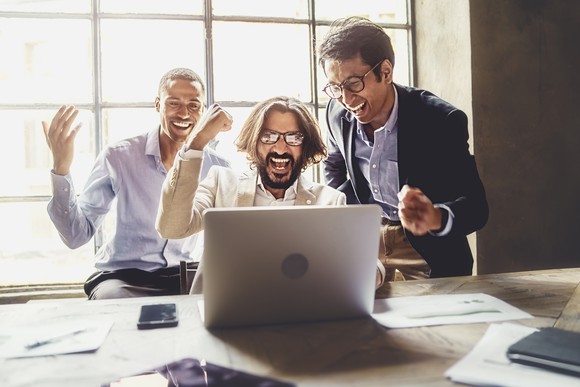People smiling in celebration around a laptop.