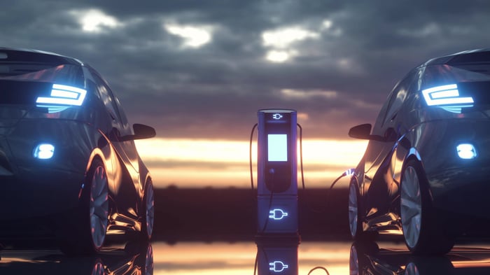 Two illuminated EVs charging at an outside charging station. 