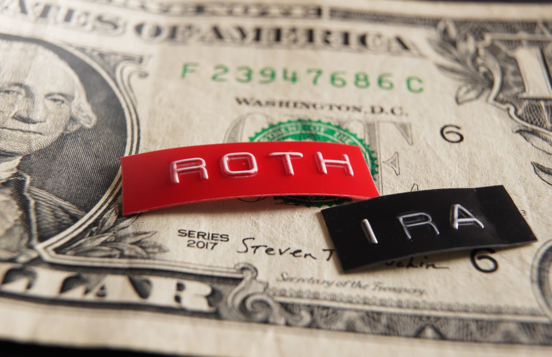 A single dollar with two labels lying on top. The red label reads, "Roth," and the black label reads "IRA." 