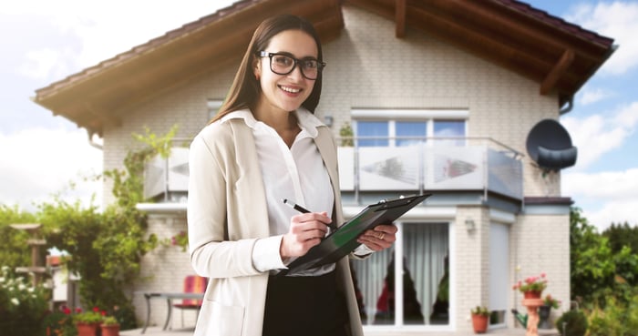 Real estate broker in front of a house with a clipboard. 